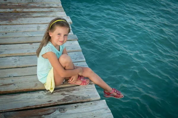 Cute girl in summer outfit staing on a pier near the sea — Stock Photo, Image