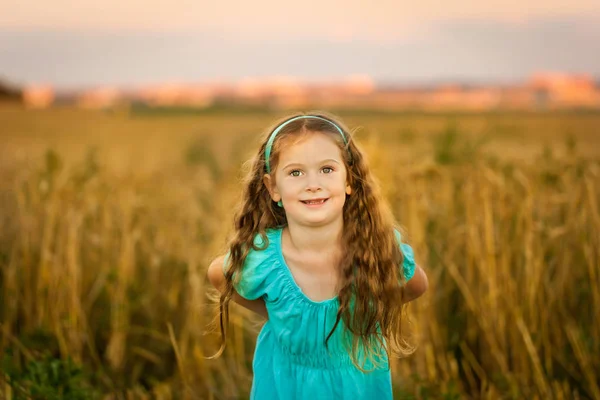 Menina feliz no campo de trigo na noite de verão quente e ensolarado — Fotografia de Stock