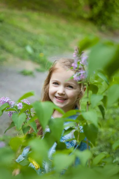 Linda niña sonriente cerca de un arbusto de flor lila —  Fotos de Stock