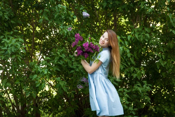 Hermosa mujer en un vestido azul de verano con flores lila en un jardín floreciente. Flor de primavera . — Foto de Stock