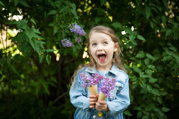 Маленька дівчинка з вафельним конусом морозива, наповненим бузковими квітами в руках — стокове фото