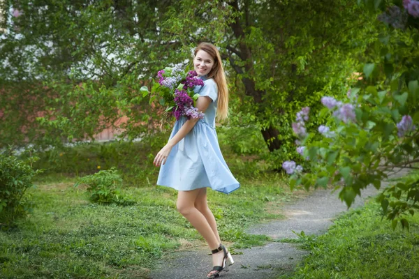 Hermosa mujer en un vestido de verano azul con flores lila en una b — Foto de Stock