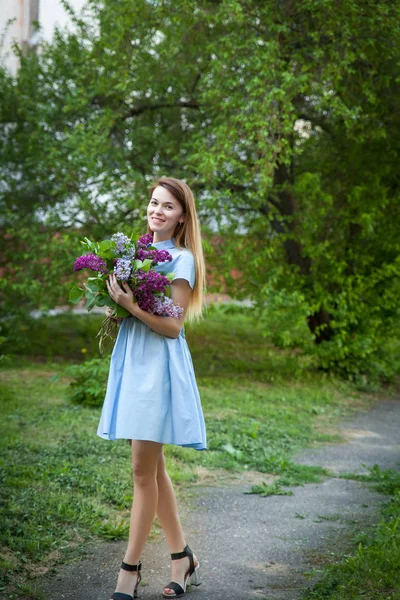 Hermosa mujer en un vestido de verano azul con flores lila en una b — Foto de Stock