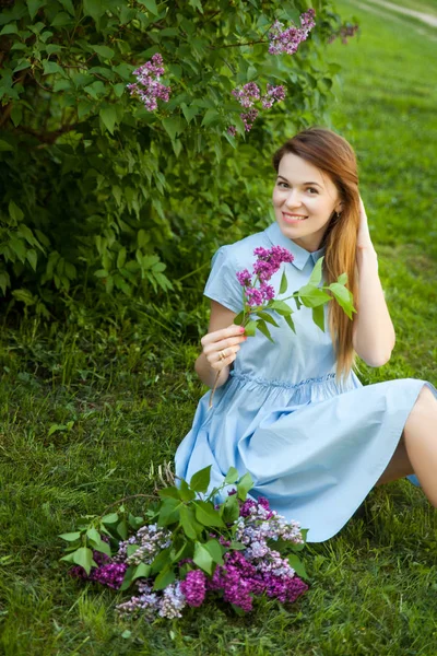 Joven mujer hermosa con el pelo rojo se sienta en una hierba bajo el árbol lila y disfruta de su vida — Foto de Stock