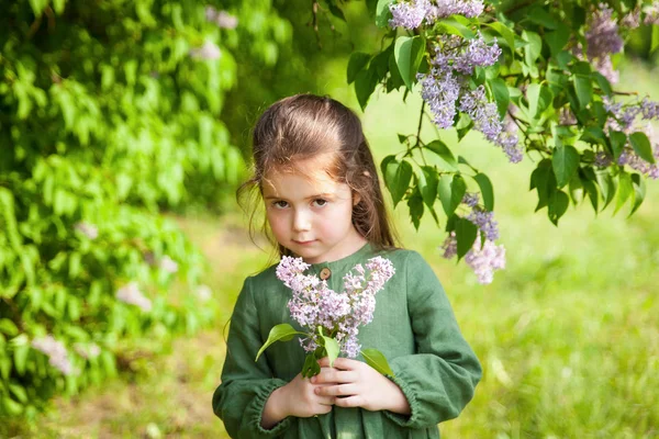 Yeşil Keten Elbiseli Tatlı Kız Parkta Çiçek Açan Leylaklarla Eğleniyor — Stok fotoğraf