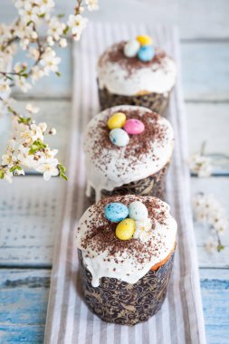 Paskalya pastası kulich. Geleneksel Paskalya tatlı ekmeği şeker jöleli ve şeker kamışlı yumurta ve çikolata parçacıklarıyla süslenmiş. Arka planda Paskalya Ortodoks pastası ve kiraz çiçeği dalı