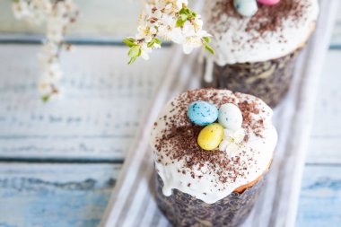 Paskalya pastası kulich. Geleneksel Paskalya tatlı ekmeği şeker jöleli ve şeker kamışlı yumurta ve çikolata parçacıklarıyla süslenmiş. Arka planda Paskalya Ortodoks pastası ve kiraz çiçeği dalı
