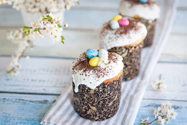 Easter cake kulich. Traditional Easter sweet bread decorated with sugar glaze and candy cane shape eggs and chocolate chips. Easter orthodox cake and cherry blossom twig in the background