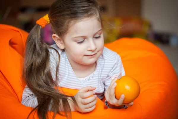 소녀는 오렌지 열매가 오렌지 의자에 걸으고 귀여운 집에서 즐겁게 있습니다 — 스톡 사진