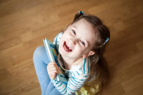 床に座って本を持っている子供のトップビュー 笑顔の就学前の女の子とともにおとぎ話の本 — ストック写真