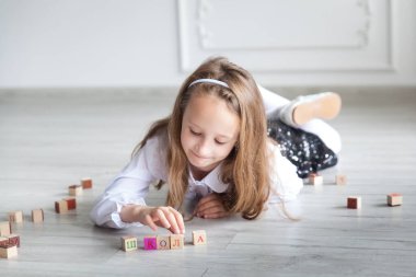 Ahşap zeminde, üzerinde renkli ahşap harflerle üniformalı bir kız öğrencinin portresi. Okula dönelim. Evden uzaklık öğrenme
