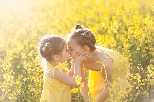 Cute girls in yellow dresses having fun in the field of flowering rape. Nature blooms rape seed field. Summer holidays
