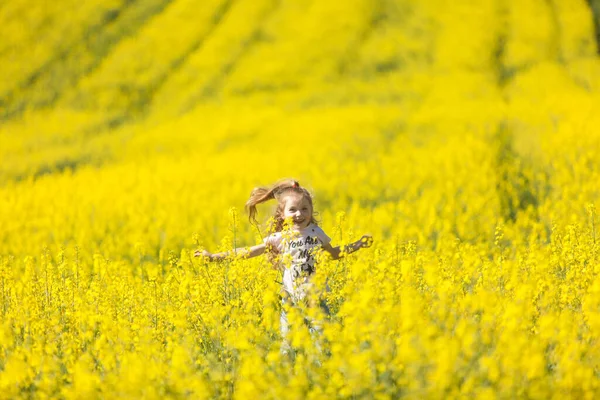 Cute girl having fun in the field of flowering rape. Nature blooms rape seed field. Summer holidays