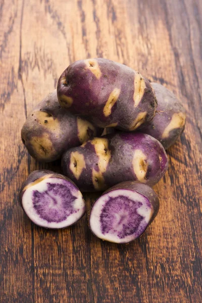 White - violet potato on wooden background. Organic plant Royaltyfria Stockbilder