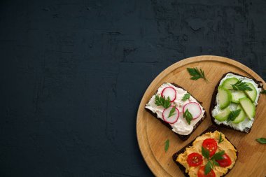 Saf peynir, humus, avokado, turp ve domatesli sağlıklı vejetaryen çavdar ekmekli sandviç. Siyah arkaplan üzerinde tahta tahta tahta, kopyalama alanı, üst görünüm