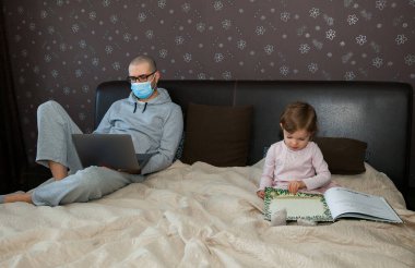 Korunaklı maskeli baba karantina sırasında Coronavirus 'ta çalışıyor. Çocuk evde, anaokulu kapalı. Kızı kitabı okuyor..