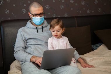 Korunaklı maskeli baba karantina sırasında Coronavirus 'ta çalışıyor. Çocuk evde, anaokulu kapalı. Kızı ona dizüstü bilgisayarda yardım ediyor..