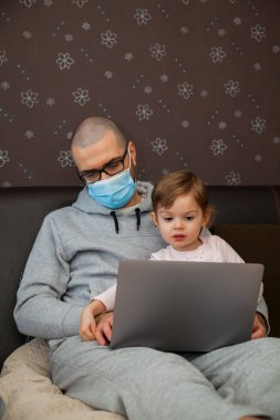 Korunaklı maskeli baba karantina sırasında Coronavirus 'ta çalışıyor. Çocuk evde, anaokulu kapalı. Kızı ona dizüstü bilgisayarda yardım ediyor..