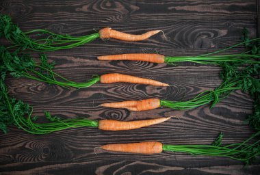 Tahta arka planda yeşil yapraklı taze olgun havuçlar. Sağlıklı vejetaryen yemeği. Düz yatıyordu