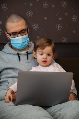 Korunaklı maskeli baba karantina sırasında Coronavirus 'ta çalışıyor. Çocuk evde, anaokulu kapalı. Kızı ona dizüstü bilgisayarda yardım ediyor..
