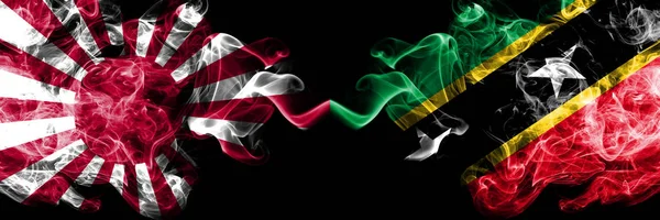 Japan rising sun naval vs Saint Kitts and Nevis smoky mystic flags placed side by side. Thick colored silky travel abstract smokes banners