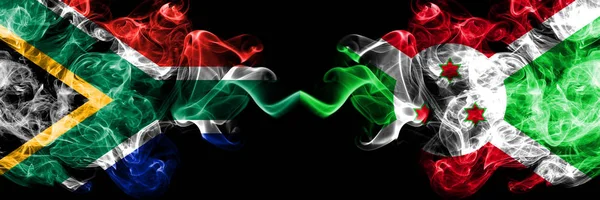 Dél-Afrika vs Burundi, burundi füstös misztikus zászlók egymás mellett. Vastag színű selymes elvont füst zászlók koncepció — Stock Fotó
