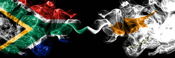 África do Sul vs Chipre, bandeiras místicas cipriotas fumegantes colocadas lado a lado. Conceito de bandeiras de fumaça abstrata sedosa de cor grossa — Fotografia de Stock