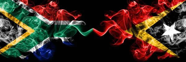 南非对东帝汶烟熏的神秘旗帜并排放置。 浓密的彩色丝状抽象烟旗概念 — 图库照片