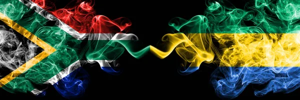 Dél-Afrika vs Gabon, gaboni füstös misztikus zászlók egymás mellett. Vastag színű selymes elvont füst zászlók koncepció — Stock Fotó