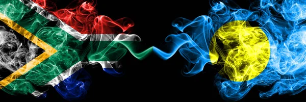 Dél-Afrika vs Palau, Palaulan füstös misztikus zászlók egymás mellett. Vastag színű selymes elvont füst zászlók koncepció — Stock Fotó