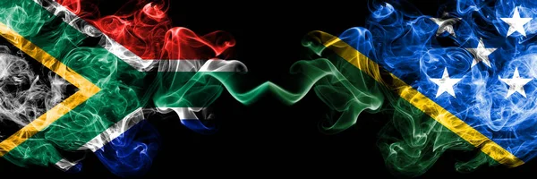 South Africa vs Solomon Islands smoky mystic flags placed side by side. Thick colored silky abstract smoke flags concept