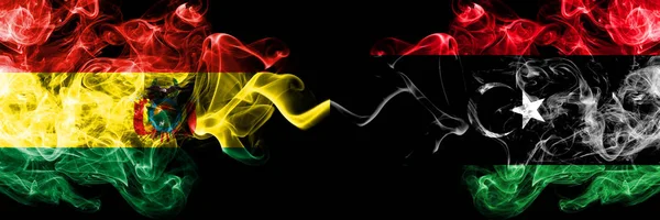 Bolívia, bolíviai vs Líbia, líbiai füstös misztikus államok zászlói egymás mellett. Koncepció és ötlet vastag színű selymes elvont füst zászlók — Stock Fotó