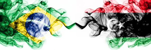 Бразилія, Бразилія проти Лівії, лівійські димові містичні прапори розміщені пліч-о-пліч. Товсті кольорові сріблясті абстрактні димові прапори комбінують — стокове фото