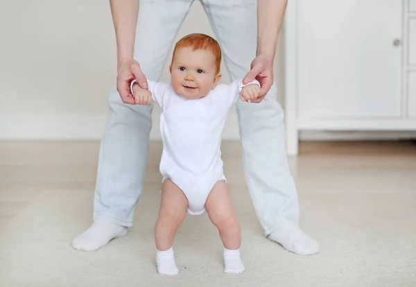 Padre y pequeño Dauther. Bebé dando los primeros pasos con la ayuda del padre en el interior del hogar Fotos De Stock