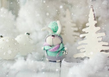 El yapımı örgü tavşan. Noel Bunny bir atkı ve şapka ile dekoratif Noel ağaçları ve topları arasında büyük bir pumpon. 