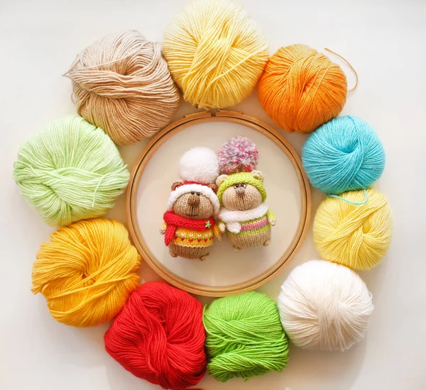 Twee gebreide beren in veelkleurige truien en hoeden met grote pompom op de achtergrond van gekleurde ballen van garen. Handgemaakte wenskaarten — Stockfoto