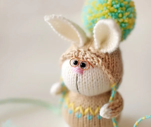 Handmade knitted toy. Easter  Bunny with glasses in beige sweater and hat with big pompom close up