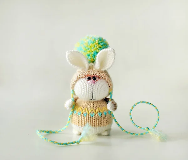 手工针织玩具。复活节兔子与眼镜在米色毛衣和帽子与大绒球关闭 图库照片