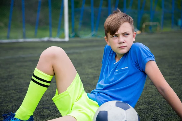 Мальчик футболист, сидящий на поле — стоковое фото