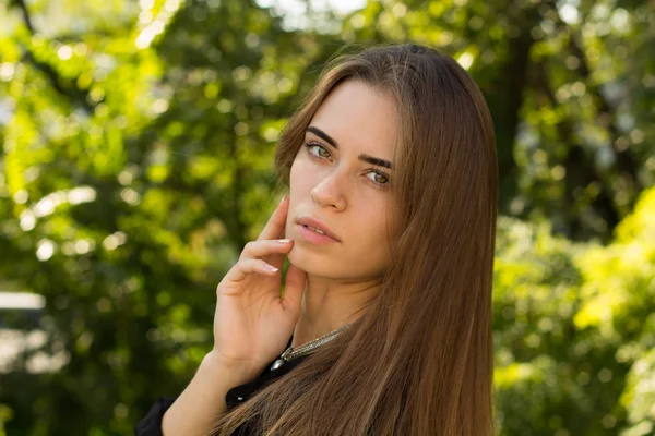 Junge Frau steht seitlich auf dem Hintergrund von Bäumen — Stockfoto