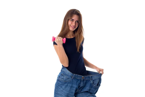 Mulher usando jeans de tamanho muito maior e segurando um halteres — Fotografia de Stock