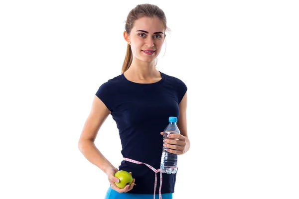 Woman with centimeter around her waist holding apple and water — 스톡 사진