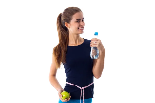 Woman with centimeter around her waist holding apple and water — 스톡 사진