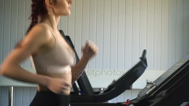 Atractiva chica caucásica corriendo en la cinta de correr en el gimnasio deportivo — Vídeo de stock