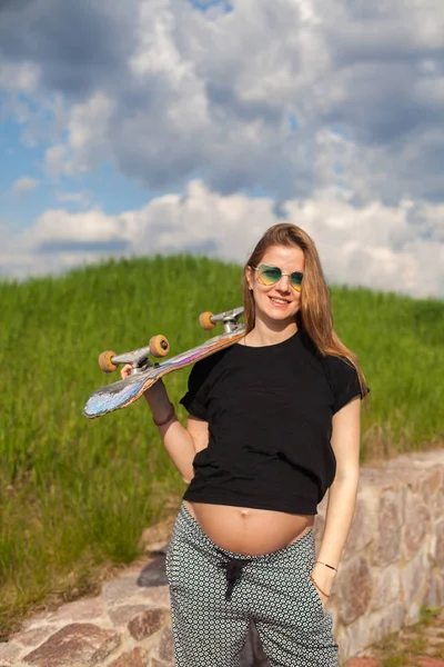 Těhotná žena držící skateboard — Stock fotografie