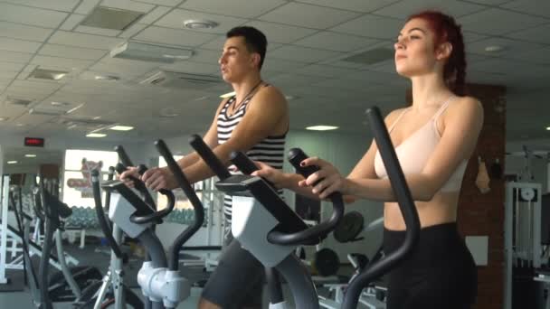Active young man and woman using elliptical machine — Stock Video