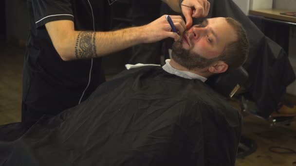 Барбермен бреет бороду человека — стоковое видео
