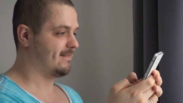 Красивый молодой человек играет в игры на смартфоне — стоковое видео