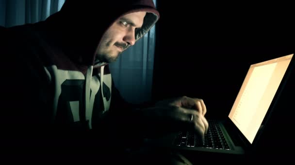 Hombre hacker en una capucha trabaja en una computadora — Vídeos de Stock