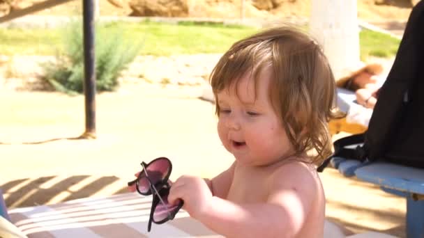 Baby flicka sitter med solglasögon i händer — Stockvideo